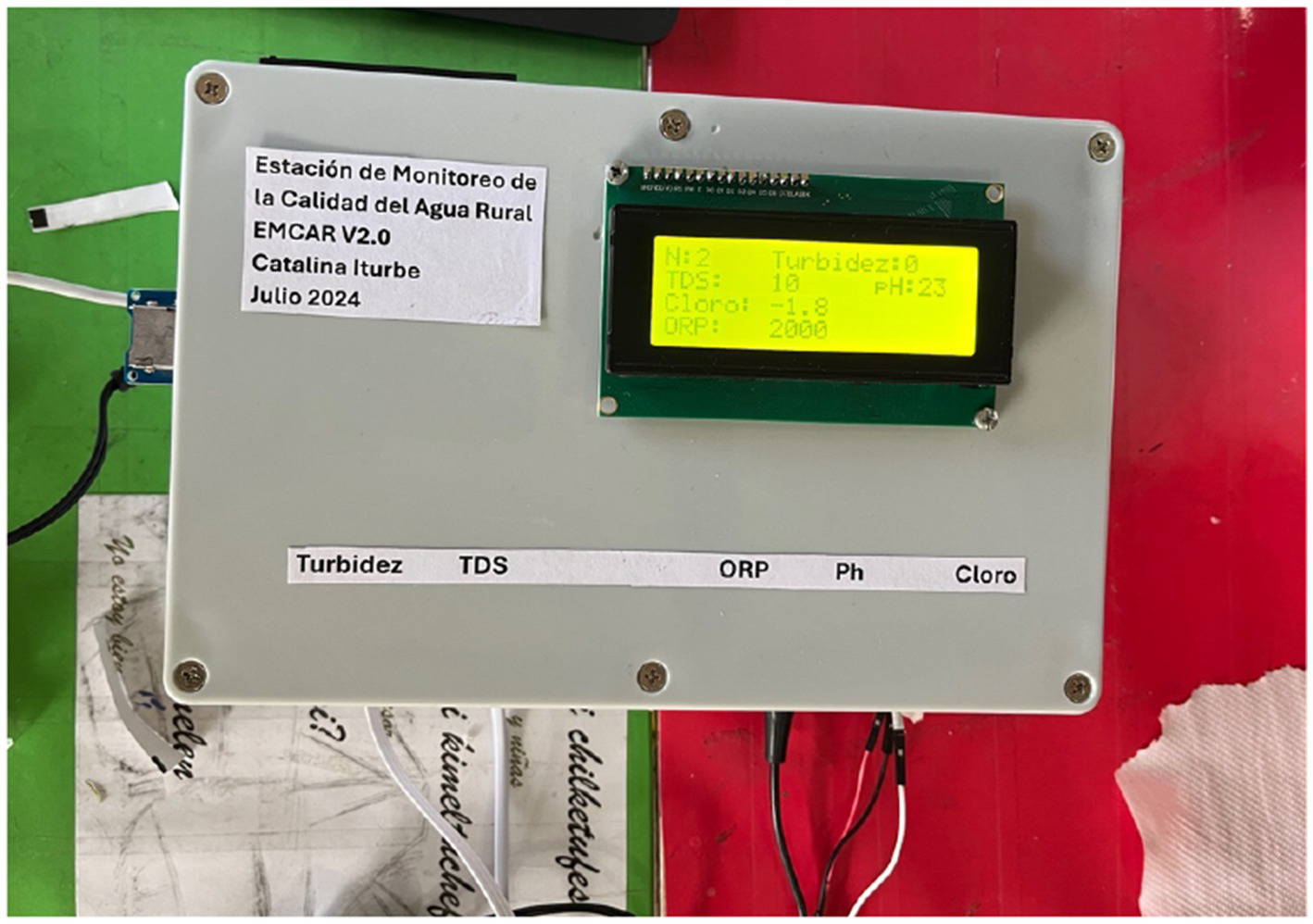 Water quality monitoring device labeled "Estación de Monitoreo de la Calidad del Agua Rural." Display shows measurements: Turbidez: 0, TDS: 10, Cloro: -1.8, PH: 23, ORP: 2000. Labeled sections include Turbidez, TDS, ORP, PH, and Cloro.