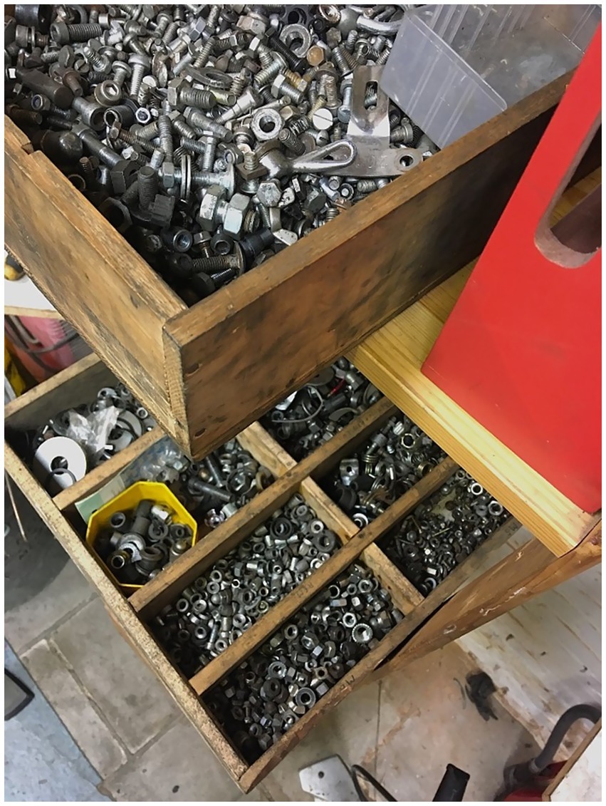 The picture shows wooden drawers filled with various metal nuts, bolts, and hardware. The top drawer contains a mix of different sizes and types of fasteners, while the lower drawer has neatly organized compartments for smaller componentry. This is just a small selection of all the stored reusable parts and components.