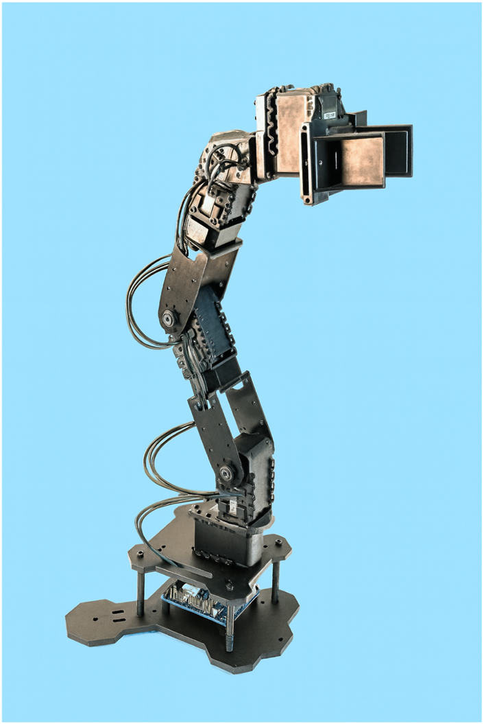A robotic arm with multiple joints and cables is mounted on a black base against a blue background. The arm has a rectangular attachment at the end.