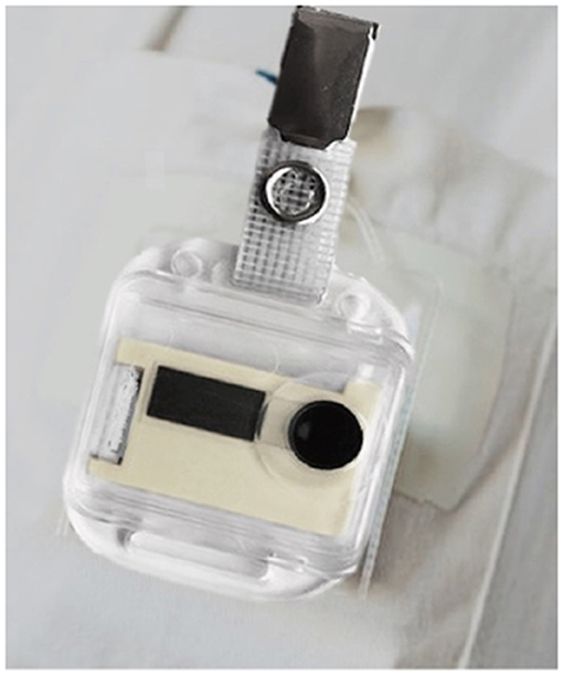 Wearable electronic device with a transparent casing and black components, attached to fabric using a metallic clip.