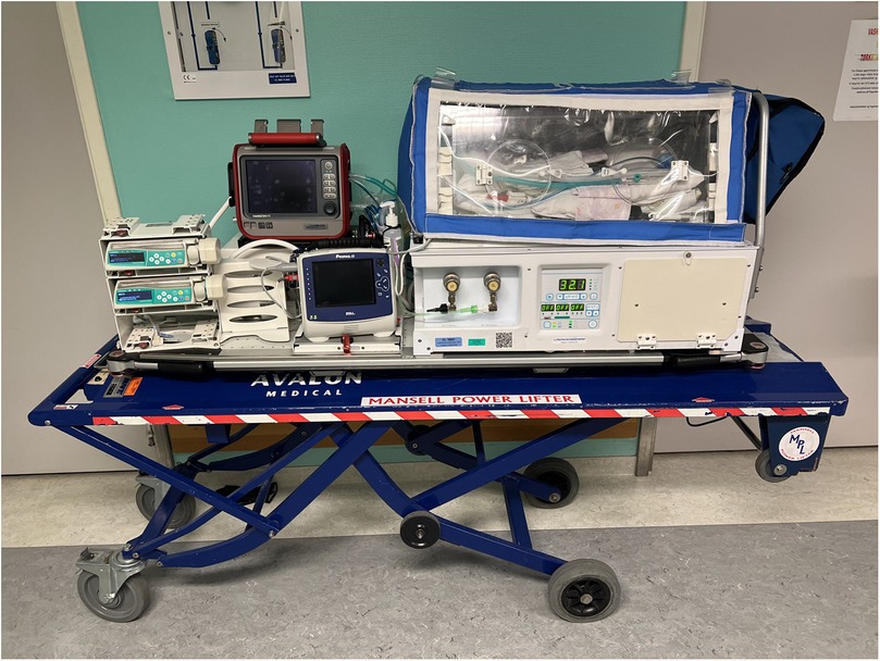 Medical transport incubator equipped with monitoring devices and control panels, mounted on a blue trolley labeled \