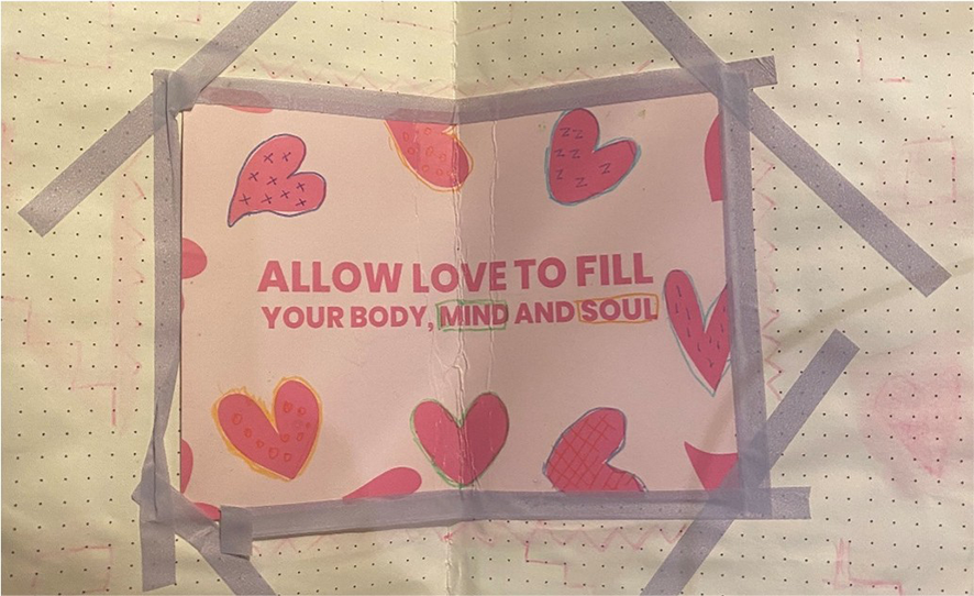 Photograph of an open sketchbook, with a poster stuck into this with washy tape. The poster is pink with hearts drawn on it, and writing that says ‘allow love to fill your body, mind and soul’.