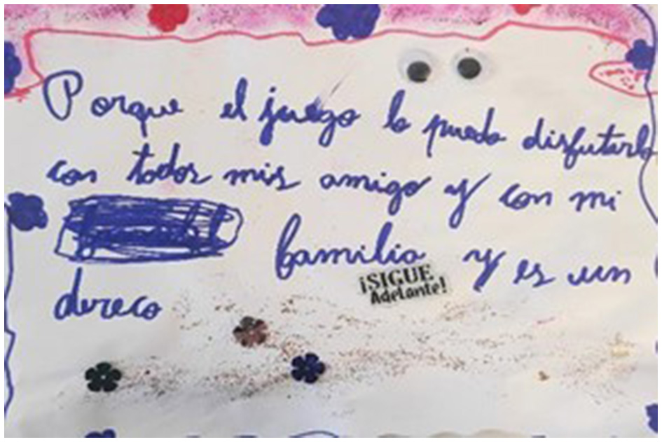 Handwritten text in Spanish on decorated paper “Porque el juego lo puedo disfrutar con todos mis amigos y con mi familia y es un derecho” Translation: “Because I can enjoy play with all my friends and my family and it is a right.” The paper has colorful flower drawings and a small sticker saying “¡SIGUE Adelante¡ (Keep Going!)”.