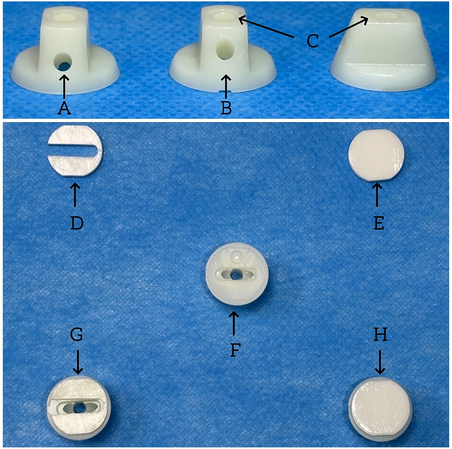 Three three-dimensional plastic components labeled A, B, and C are positioned in a row on a blue surface. Each component has a cylindrical shape with a small hole near the base. Below, smaller circular parts labeled D, E, F, G, and H are arranged with arrows indicating connection or assembly points.