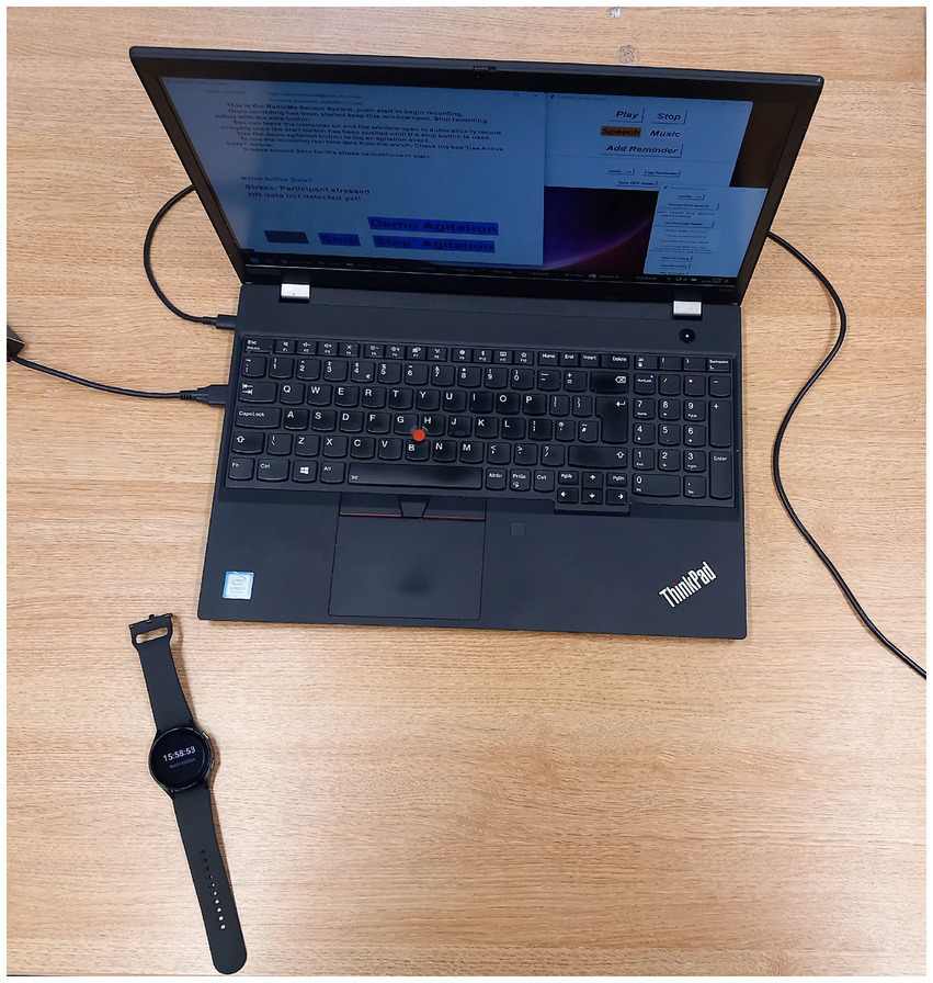 A laptop displaying text and options is connected to cables on a wooden surface. Next to it lies a black smartwatch showing the time "15:58:51".