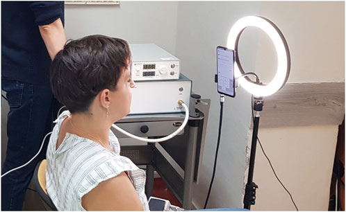 A person sits in front of a smartphone on a tripod surrounded by a ring light.