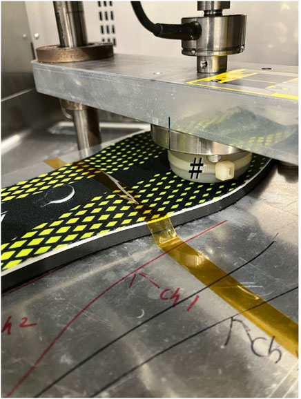 A close-up of a machine pressing a material with a black and yellow diamond pattern. A white roller with the symbol