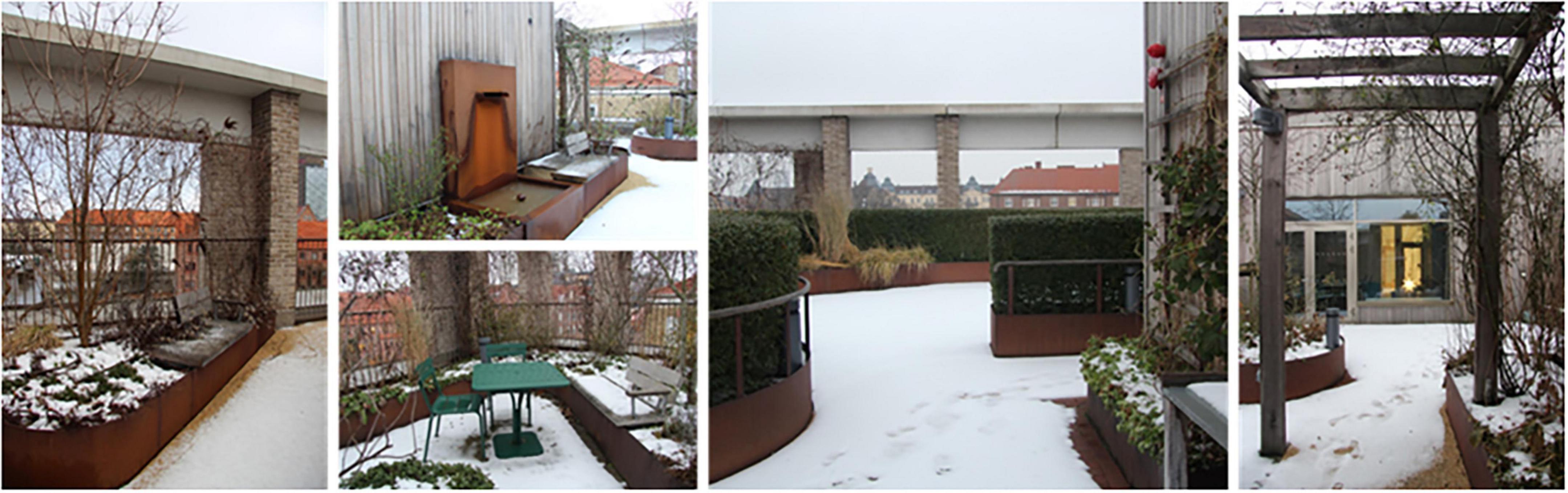 Snow-covered rooftop garden featuring a variety of planters, brick columns, and modern architectural elements. Green foliage peaks through the snow, and a green patio table and chairs are visible. The structure includes exposed metal and a wooden pergola, framing some of the scenic views of distant rooftops under cloudy skies.