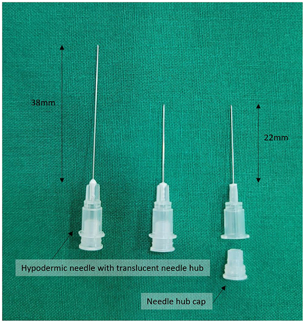Three hypodermic needles with translucent hubs shown on a green surface. Two needles are 38 millimeters long, and one is 22 millimeters. A detached needle hub cap is also present.
