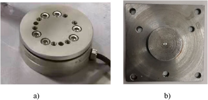 Image showing two metal components. Left (a) is a cylindrical device with a circular arrangement of screws and openings on top, with an attached cable. Right (b) is a flat, square metal plate with a protruding circular section in the center, featuring four corner holes.