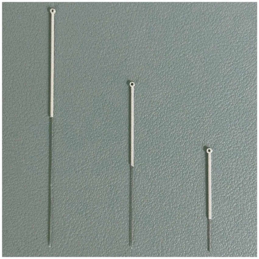 Three metal needles of varying lengths displayed vertically on a textured gray surface. The needles have loops at one end, suggesting they may be used for specific medical or industrial purposes.