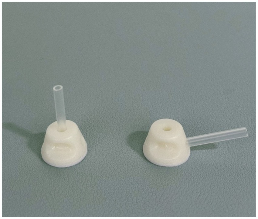 Two white plastic parts with cylindrical extensions are displayed on a gray surface. The part on the left has a vertical extension, while the part on the right has a horizontal one.