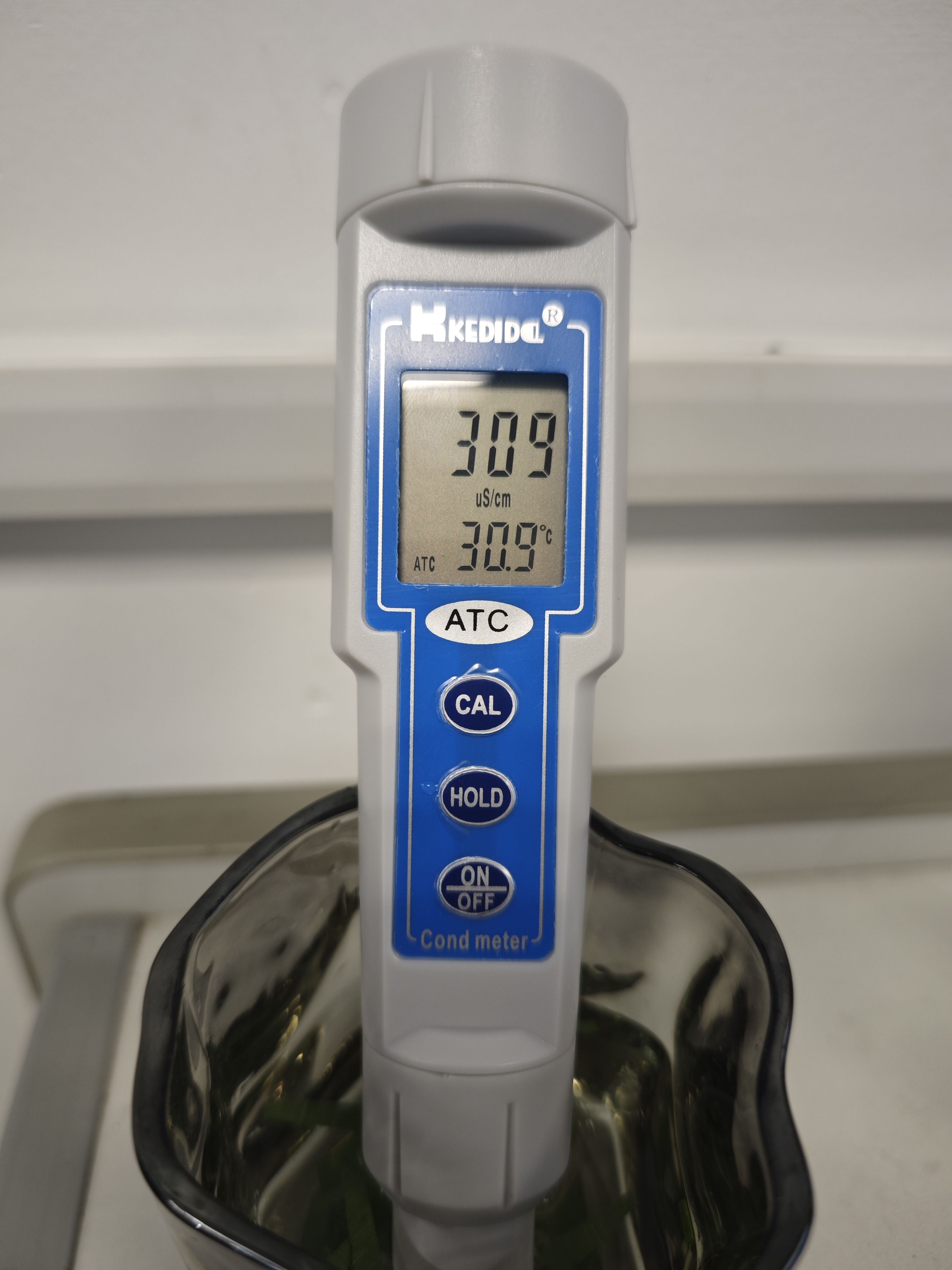 Digital conductivity meter displaying a reading of three hundred nine microsiemens per centimeter and a temperature of thirty point nine degrees Celsius. It is partially submerged in a container.