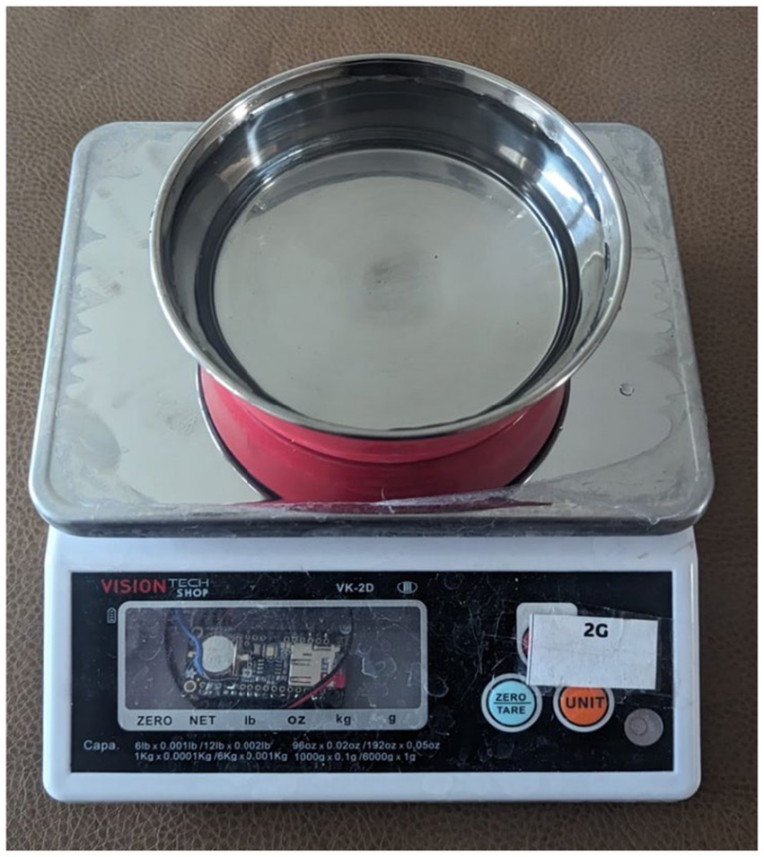 A digital kitchen scale with a metallic bowl on top. The scale displays buttons labeled