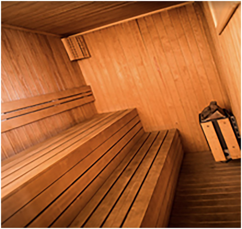 Wooden sauna interior with two-tiered benches along the left wall, a heater with stones on the right, and wooden paneling on the walls and ceiling.