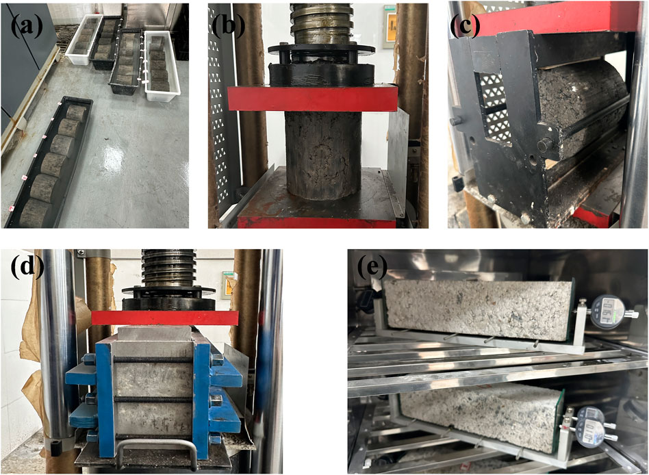 (a) Concrete cylinder molds in tubs on the floor. (b) A cylindrical concrete sample under compression testing. (c) A cylindrical sample in a flexural test machine. (d) A cubical concrete sample in a compression machine. (e) A concrete beam in a testing setup with gauges attached.
