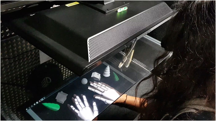 Person looking at virtual hands overlaid on their real hands through a glass pannel. Real and virtual objects are visible around the hands.